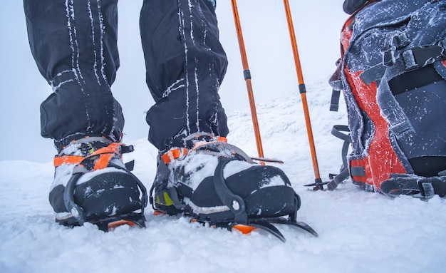 Hombre vestido con crampones de pie junto a la mochila y bastones de trekking en la nieve profunda