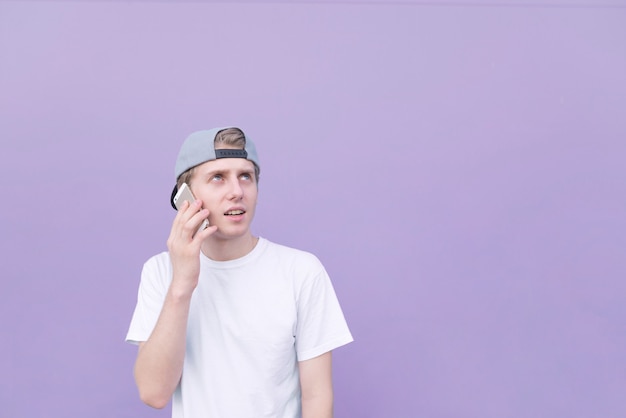 Hombre vestido con una gorra y una camiseta blanca habla sobre un fondo morado