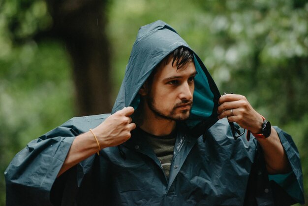 Hombre vestido con un impermeable poniéndose la capucha en medio de un bosque