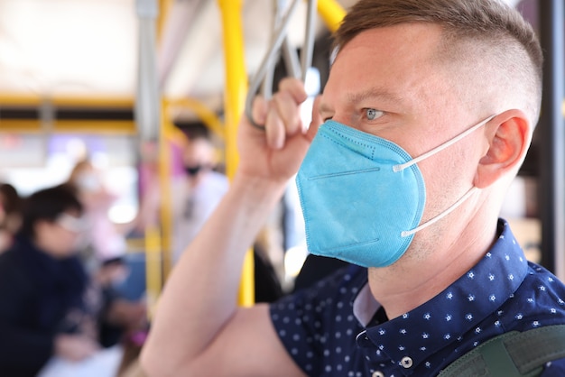 Hombre vestido con máscara médica protectora montando autobús y aferrándose a la barandilla