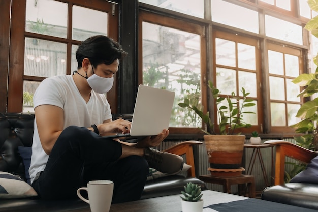 Hombre vestido con mascarilla está trabajando con un portátil en un café