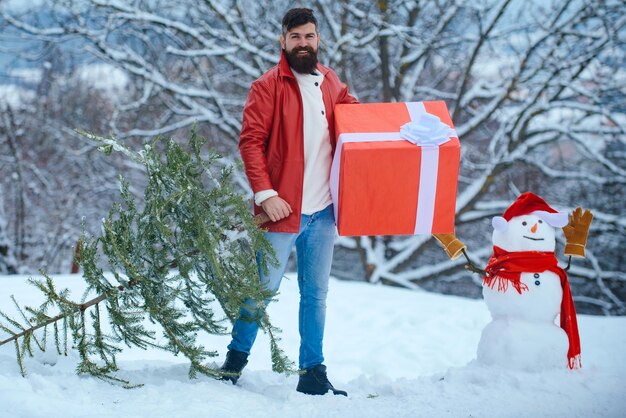 Hombre vestido de Navidad con regalo cerca del fondo de Navidad. Padre feliz con regalo de Navidad sobre fondo de muñeco de nieve de invierno.