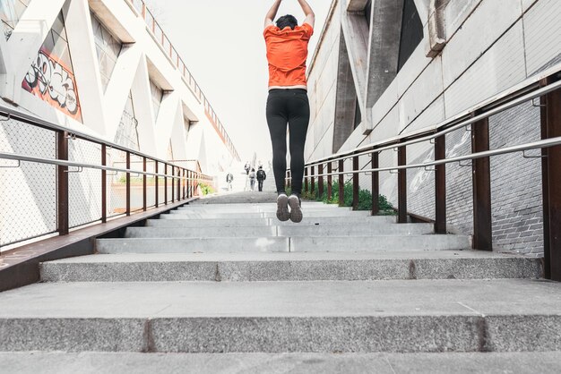 Foto hombre vestido con ropa deportiva saltando mientras sube unas escaleras en la calle