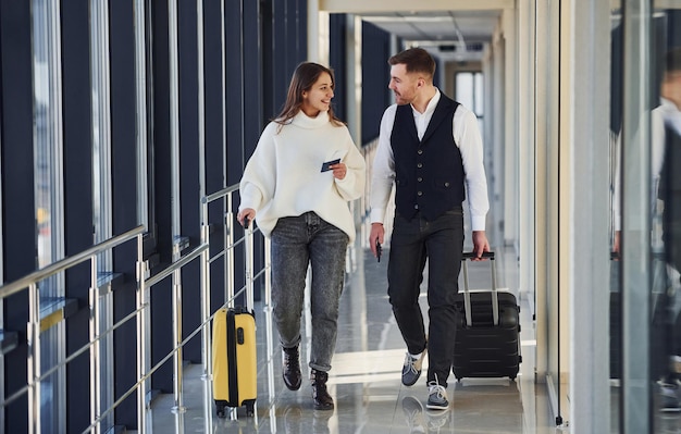 Hombre vestido con ropa elegante y formal caminando con una mujer joven en el interior del aeropuerto.