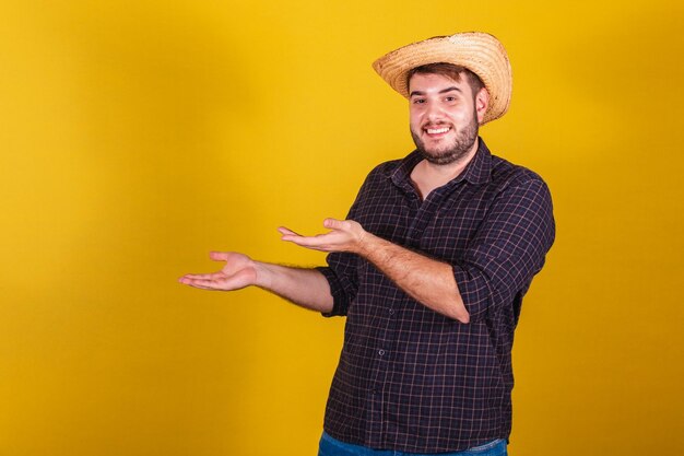 Hombre vestido con ropa típica de Festa Junina Fiesta de Arraia de Sao Joao presentando algo con sus manos