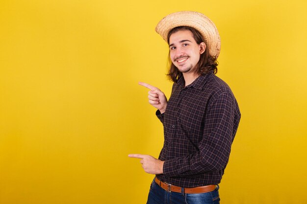 Hombre vestido con ropa típica para la fiesta Junina Señalando el lado izquierdo con los dedos espacio para publicidad y texto