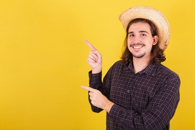 Hombre vestido con ropa típica para la fiesta Junina Señalando el lado izquierdo con los dedos espacio para publicidad y texto