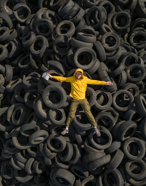 Foto hombre vestido con una sudadera con capucha amarilla sobre un vertedero colosal de neumáticos de automóviles que simboliza el problema de los residuos y la contaminación la perspectiva del hombre proporciona una sensación de escala en la extensión del vertedero de neumáticos