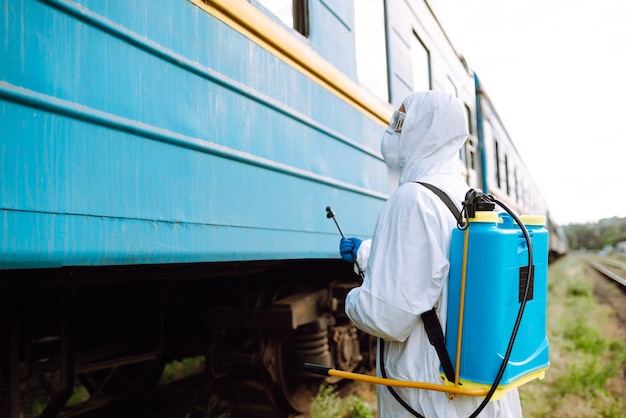 Hombre vestido con traje de protección público desinfectando un tren.