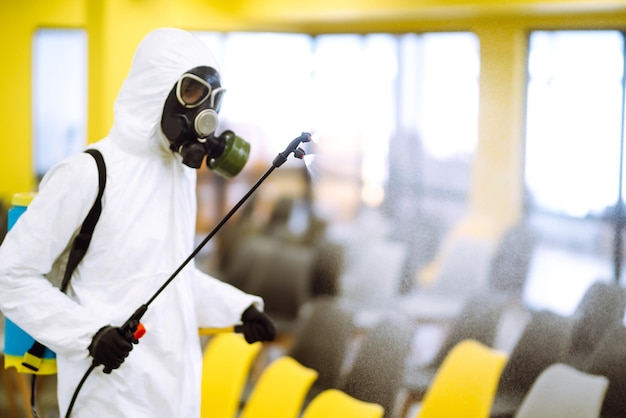Foto hombre vestido con traje protector que desinfecta el salón de actos con productos químicos en aerosol para prevenir el coronavirus