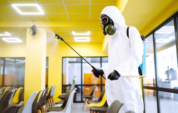 Hombre vestido con traje protector que desinfecta el salón de actos con productos químicos en aerosol para prevenir el coronavirus