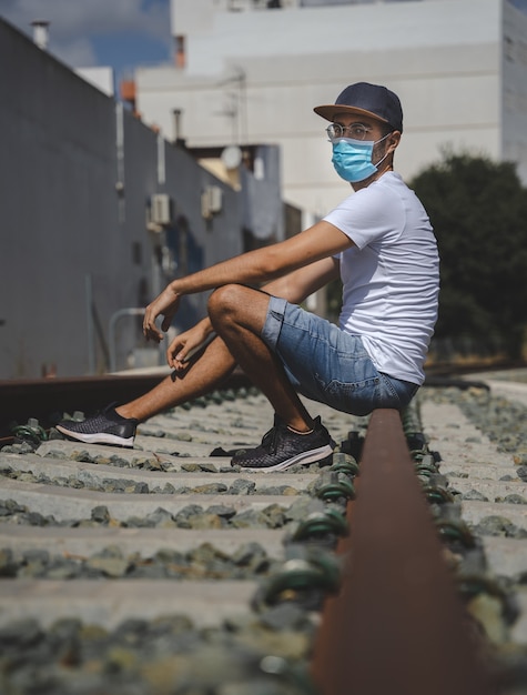 Hombre en la vía del tren con máscara, camiseta blanca y jeans