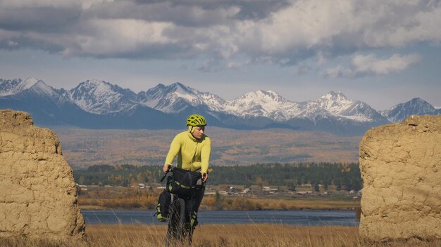 El hombre viaja en cicloturismo de terreno mixto con bikepacking El viaje del viajero con bolsas para bicicletas Sport bikepacking ropa deportiva para bicicletas en colores verdes y negros Arco de piedra cubierto de nieve de montaña