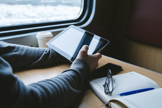 El hombre viaja en tren sentado junto a la ventana usa una tableta