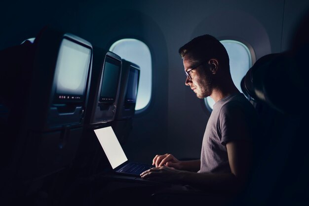 Hombre viajando en avión joven pasajero usando portátil durante vuelo nocturno