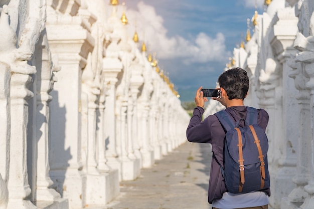 Hombre viajando con bolsa, viajero asiático tomando foto por teléfono.