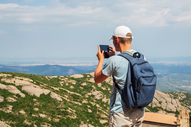 Hombre de viaje con mochila de pie, tome una foto con el teléfono inteligente Mountians Sunny day Copie el espacio