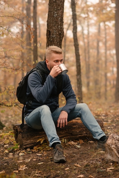 Un hombre viajero en el bosque otoñal descansa en un alto y bebe té.