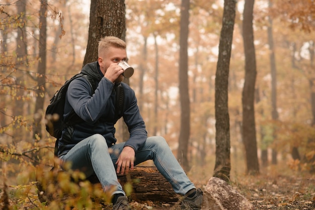 Un hombre viajero en el bosque otoñal descansa en un alto y bebe té.