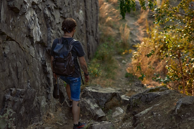 Un hombre viajero camina cerca de las rocas y el bosque otoñal sostiene un ukelele en su mano foto de alta calidad