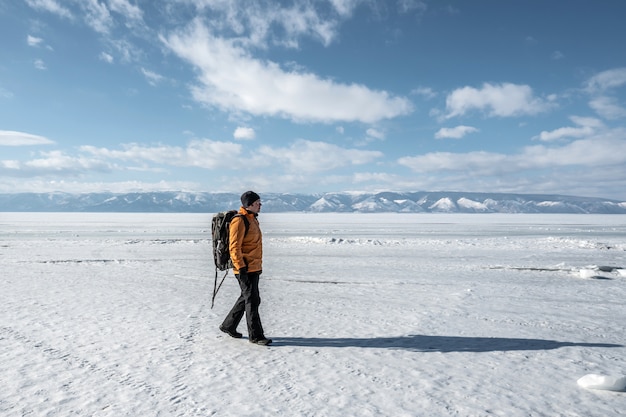 Hombre viajero camina sobre el hielo nevado del lago Baikal. Naturaleza del invierno Siberia: un lago congelado, montañas, cielo despejado