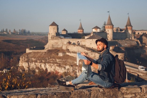 Hombre viajero con un mapa en sus manos se sienta en el fondo del antiguo castillo