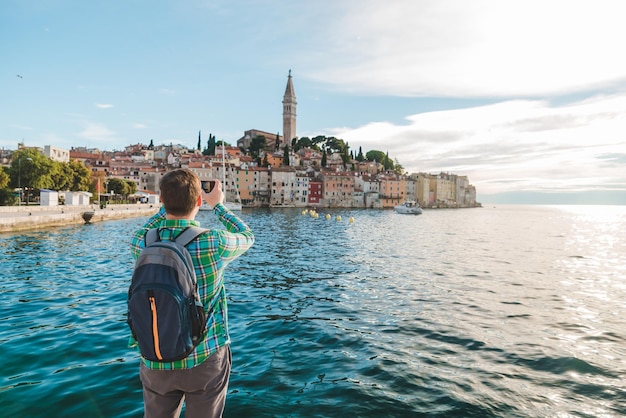 Hombre viajero mirando la ciudad de rovinj desde el puerto tomando fotos por teléfono