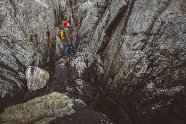 Hombre viajero con una mochila amarilla con un sombrero rojo de pie sobre fondo de rocas