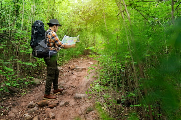 Hombre viajero con mochila y mapa buscando direcciones en el bosque