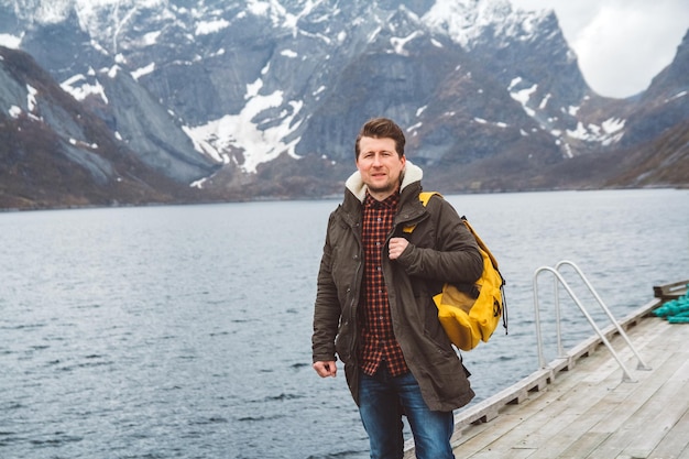 Hombre viajero con una mochila de pie sobre un muelle de madera el fondo de montañas nevadas y lago