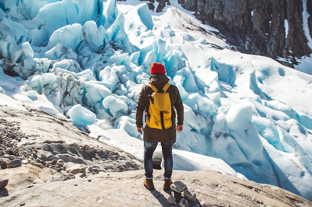 Hombre viajero con una mochila de pie sobre una roca en el fondo de un glaciar de montañas y nieve