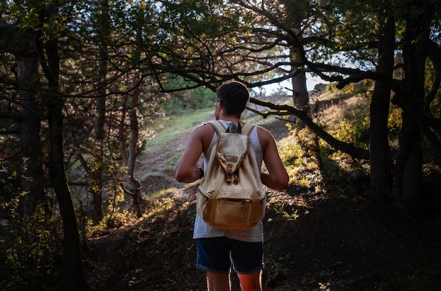 Hombre viajero con mochila de senderismo al aire libre en el bosque al atardecer de verano