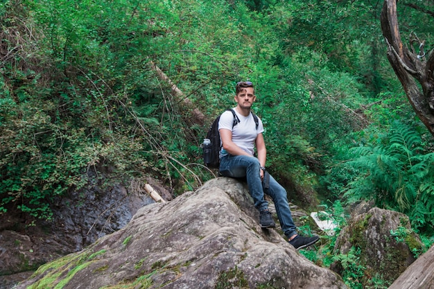 Hombre viajero con mochila sentado en roca en el bosque