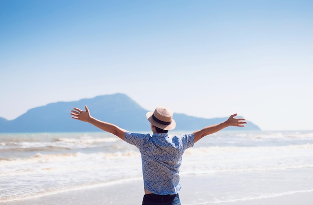 Hombre viajero parado en la playa junto al mar con montaña en el fondo de la naturalezaHermoso paisaje para viajes de aventura