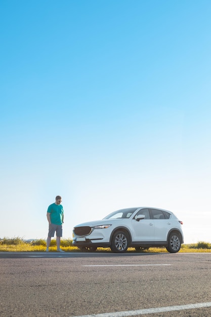 Hombre viajero de pie cerca del coche al borde de la carretera de la autopista al atardecer