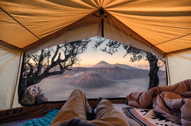 Hombre viajero relajarse y tener la vista del volcán activo Bromo dentro de una carpa en la mañana en el parque nacional Bromo Tengger Semeru, Indonesia