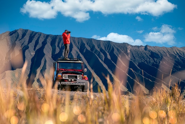 Hombre viajero toma una foto en un automóvil todoterreno vintage con montaña Bromo