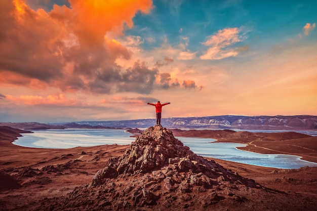 El hombre viajero usa ropa roja y levanta el brazo de pie en la cima de la montaña cerca del lago Baikal, Siberia, Rusia.