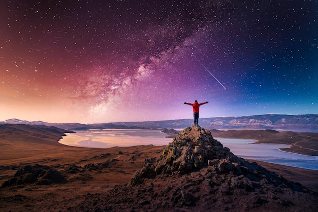 El hombre viajero usa ropa roja y levanta el brazo de pie en la montaña con la vía láctea en el lago Baikal Siberia Rusia