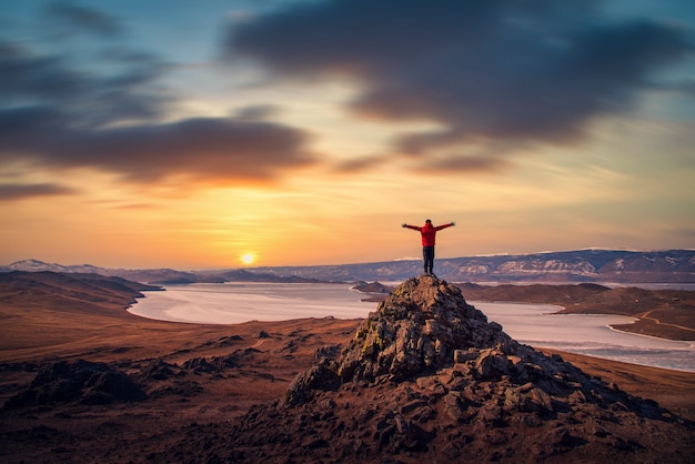 Hombre viajero usa ropa roja y levantando el brazo de pie en la montaña al atardecer en el lago Baikal, Siberia, Rusia.