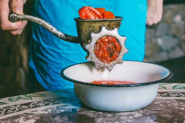 Hombre con una vieja picadora de carne hace puré de tomate