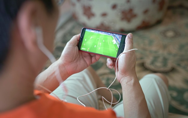 Hombre viendo fútbol y transmisión deportiva en el teléfono inteligente en casa