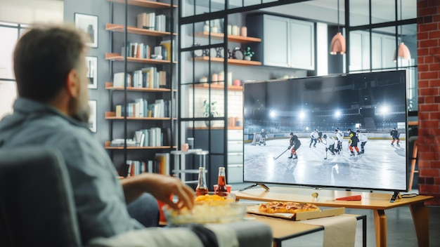 Un hombre viendo un partido de hockey en un televisor en una sala de estar.