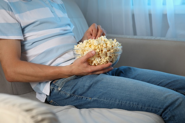 Hombre viendo la película en el sofá y comer palomitas de maíz. Comida para ver peliculas