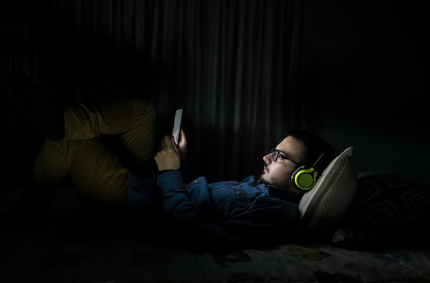 Hombre viendo series de televisión en una tableta sentada en una cama en la noche en casa