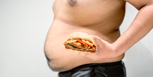 Hombre con vientre gordo sosteniendo hamburguesa en su mano