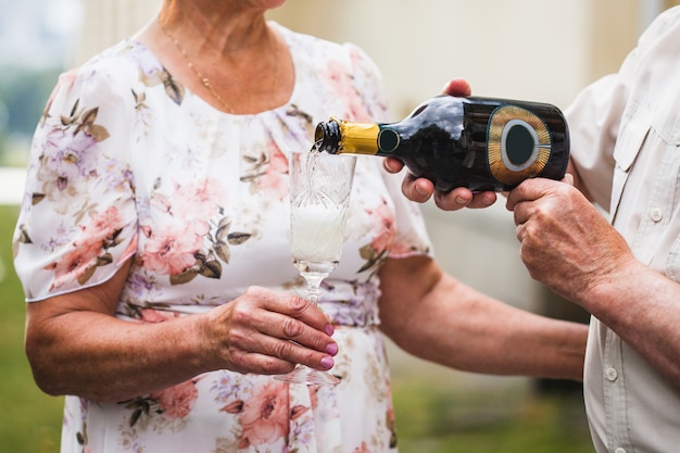 Un hombre vierte champán o vino blanco en una copa de su amada mujer, bebidas alcohólicas, celebración de aniversario, cumpleaños