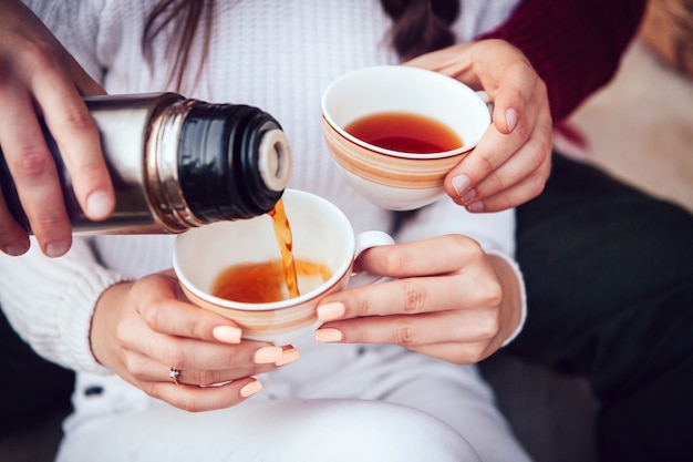 Un hombre vierte un té caliente de un termo en una taza de una niña en el otoño en la naturaleza