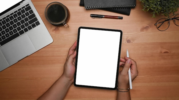 Hombre de vista superior que sostiene la tableta digital con pantalla en blanco y lápiz óptico en la mesa de madera.