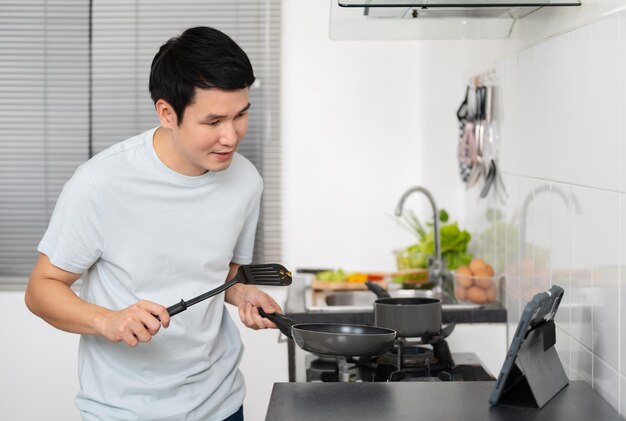 Foto hombre vlogger haciendo videollamadas desde una tableta digital mientras cocina en la cocina en casa